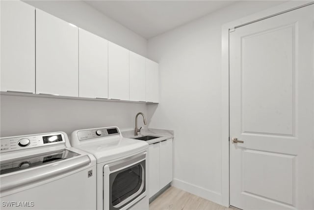 laundry room with cabinets, sink, light wood-type flooring, and washing machine and clothes dryer