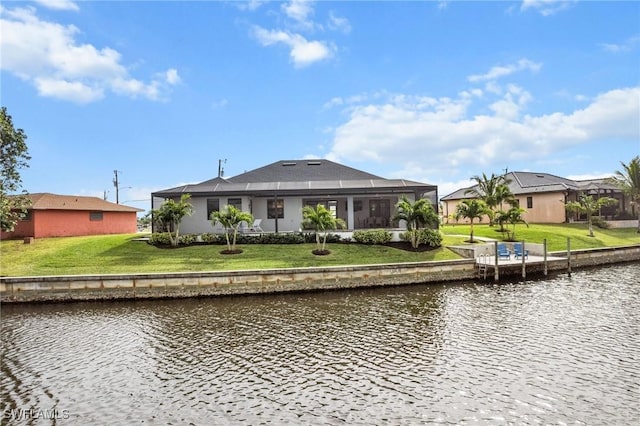 rear view of house with glass enclosure, a yard, and a water view