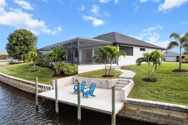 back of house featuring glass enclosure, a yard, a water view, and a patio