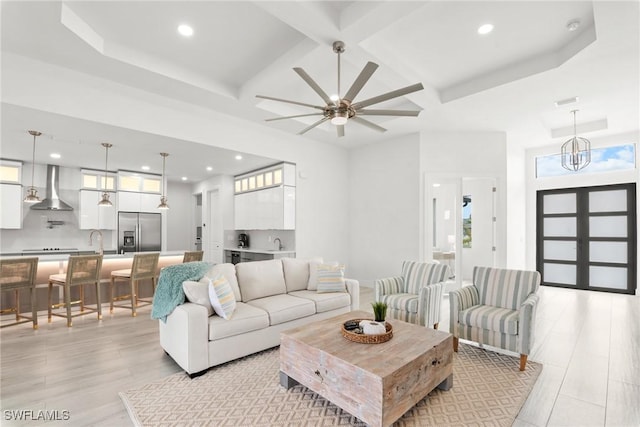 living room featuring sink, coffered ceiling, ceiling fan with notable chandelier, and beamed ceiling