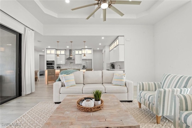 living room featuring ceiling fan, light hardwood / wood-style flooring, and a raised ceiling