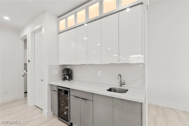 kitchen featuring sink, backsplash, white cabinets, light stone counters, and beverage cooler