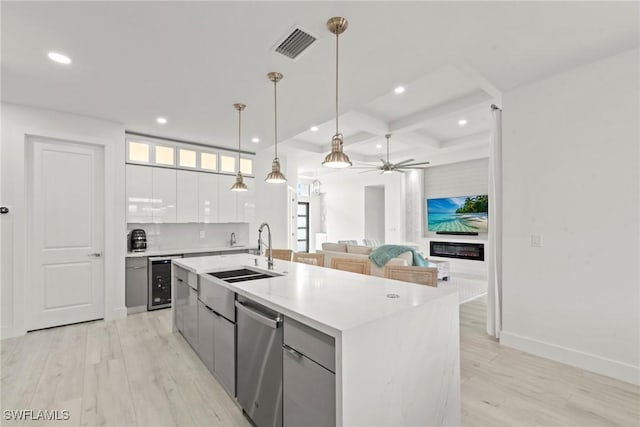 kitchen featuring stainless steel dishwasher, hanging light fixtures, sink, white cabinets, and a kitchen island with sink