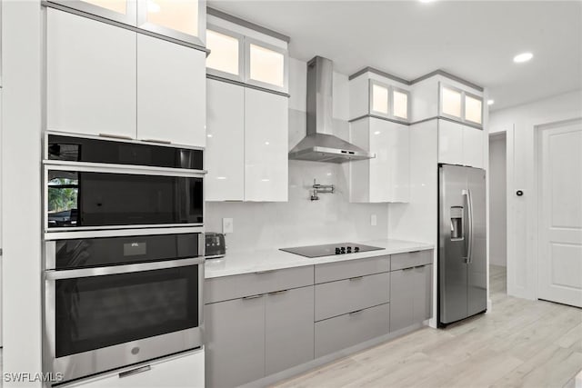 kitchen with white cabinetry, light hardwood / wood-style flooring, wall chimney range hood, and stainless steel appliances