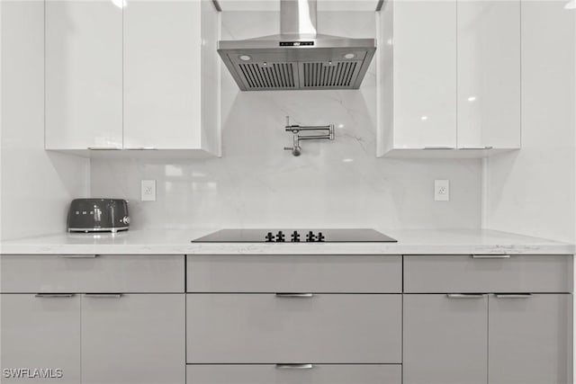 kitchen with light stone countertops, tasteful backsplash, black electric stovetop, white cabinetry, and wall chimney range hood