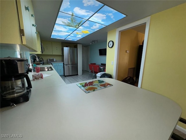 kitchen with stainless steel refrigerator, light tile patterned flooring, kitchen peninsula, and sink