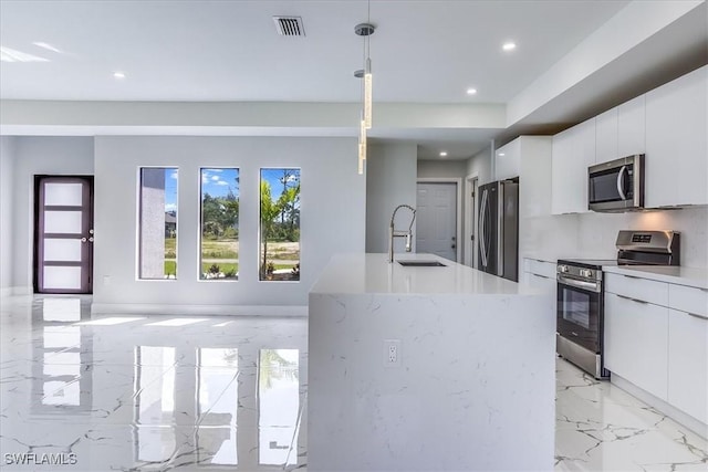 kitchen featuring pendant lighting, appliances with stainless steel finishes, white cabinetry, sink, and a kitchen island with sink