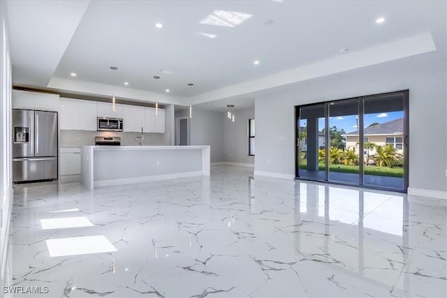 kitchen with appliances with stainless steel finishes, a tray ceiling, hanging light fixtures, a kitchen island, and white cabinets