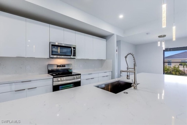 kitchen with appliances with stainless steel finishes, white cabinetry, hanging light fixtures, and sink