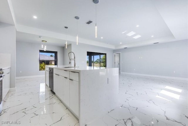 kitchen with a tray ceiling, hanging light fixtures, plenty of natural light, an island with sink, and white cabinets