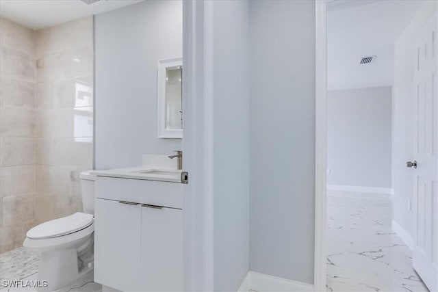 bathroom with tiled shower, vanity, and toilet