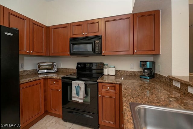 kitchen featuring light tile patterned flooring, dark stone countertops, and black appliances