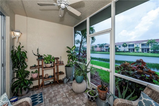 sunroom featuring ceiling fan and a water view