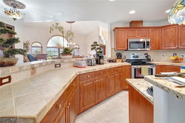 kitchen with an inviting chandelier, light tile patterned floors, pendant lighting, stainless steel appliances, and backsplash