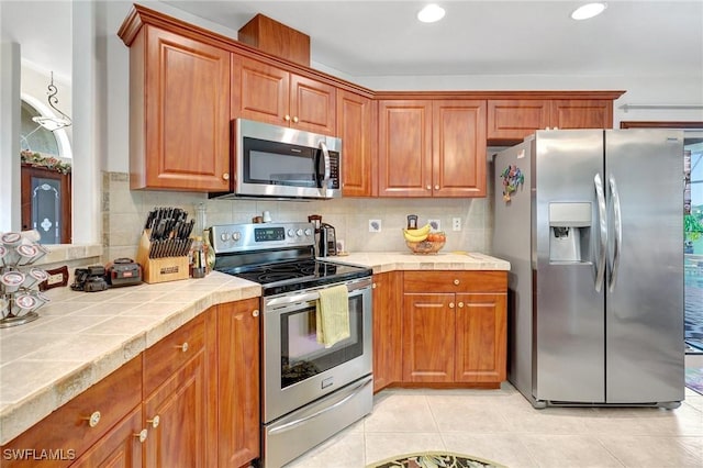 kitchen with stainless steel appliances, tasteful backsplash, tile counters, and light tile patterned floors