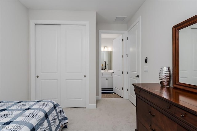 bedroom featuring ensuite bath, a closet, and light carpet