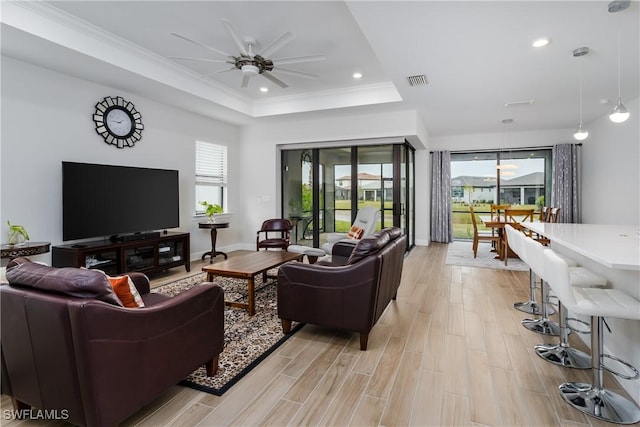 living room with a raised ceiling, ceiling fan, light wood-type flooring, and a healthy amount of sunlight