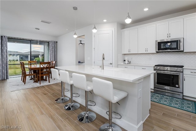 kitchen with white cabinets, appliances with stainless steel finishes, pendant lighting, and a kitchen island with sink