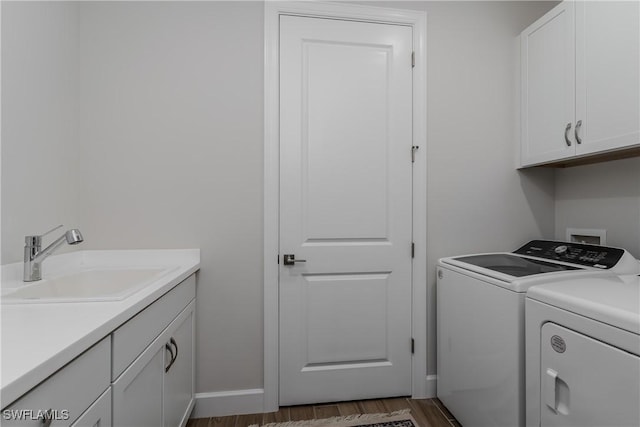 clothes washing area with sink, washing machine and dryer, cabinets, and dark hardwood / wood-style floors