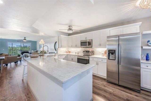 kitchen with wood-type flooring, white cabinetry, appliances with stainless steel finishes, and hanging light fixtures