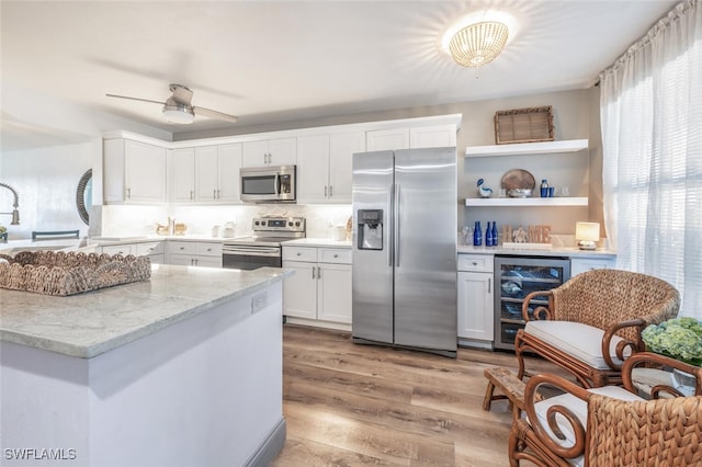 kitchen featuring appliances with stainless steel finishes, wine cooler, white cabinets, light stone countertops, and light wood-type flooring