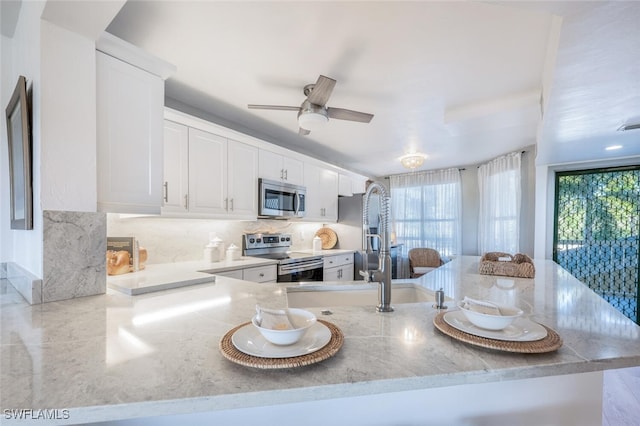 kitchen featuring ceiling fan, stainless steel appliances, a healthy amount of sunlight, white cabinets, and kitchen peninsula