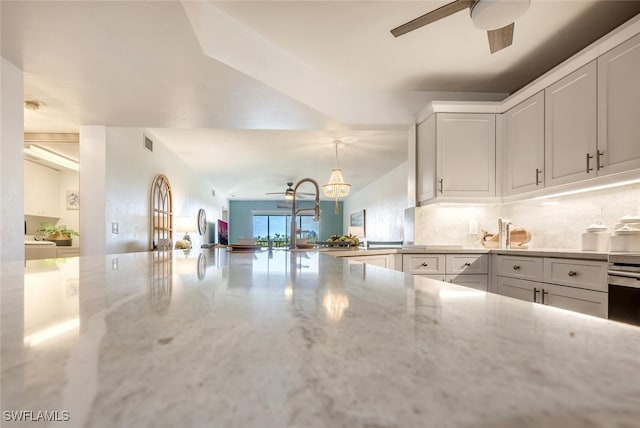 kitchen with decorative light fixtures, backsplash, sink, light stone countertops, and white cabinets