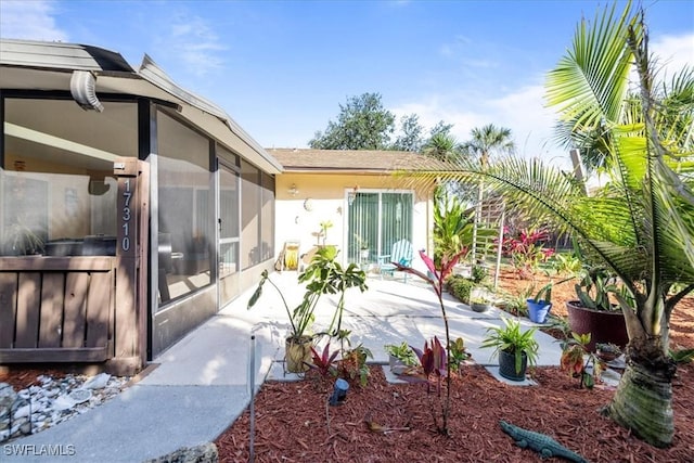 exterior space with a patio area, stucco siding, a shingled roof, and a sunroom