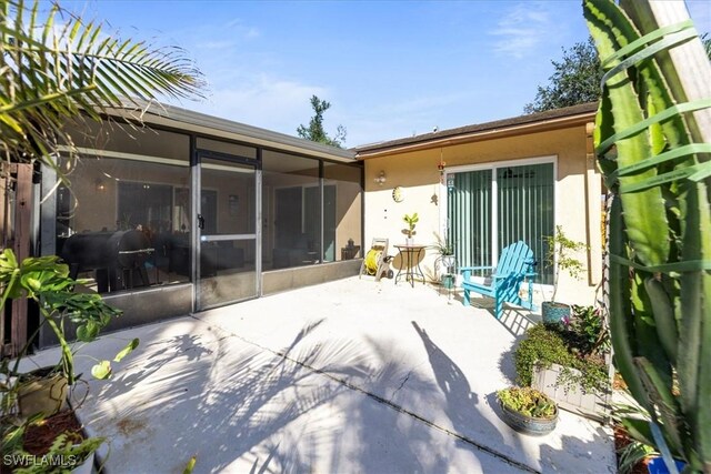 rear view of property with a patio area, a sunroom, and stucco siding