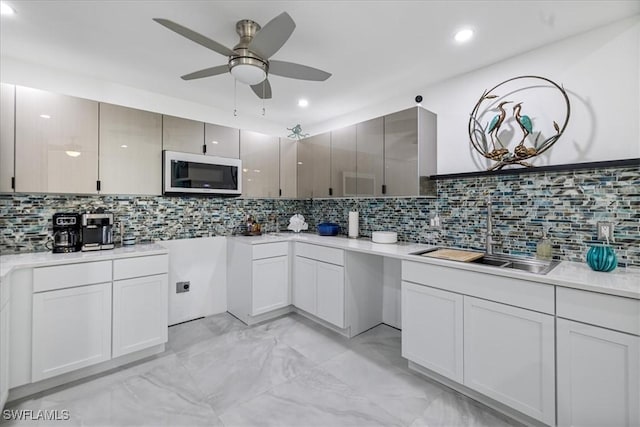 kitchen featuring decorative backsplash, light countertops, a ceiling fan, and a sink