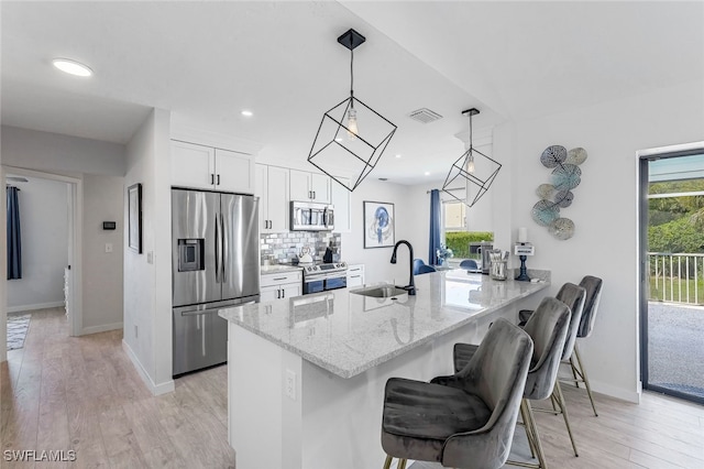 kitchen with decorative light fixtures, kitchen peninsula, sink, stainless steel appliances, and white cabinets