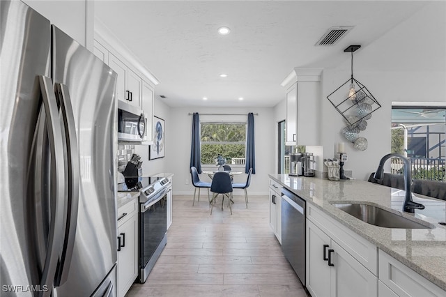 kitchen with decorative light fixtures, sink, stainless steel appliances, and white cabinetry