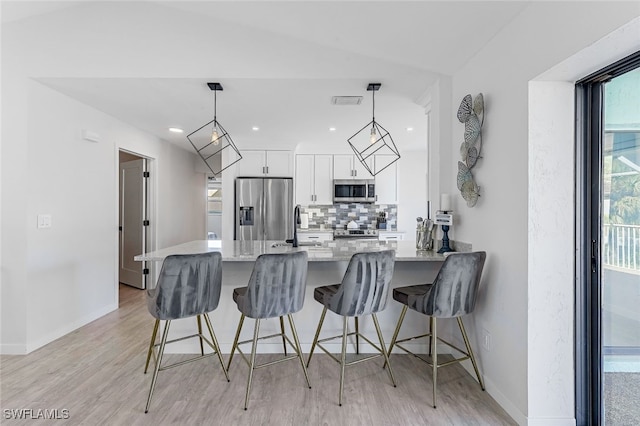 kitchen featuring pendant lighting, appliances with stainless steel finishes, white cabinetry, tasteful backsplash, and a breakfast bar area