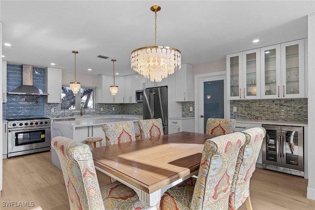 dining space with light hardwood / wood-style floors, beverage cooler, and an inviting chandelier