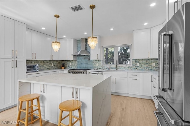 kitchen featuring wall chimney range hood, a center island, a kitchen bar, white cabinetry, and high end fridge