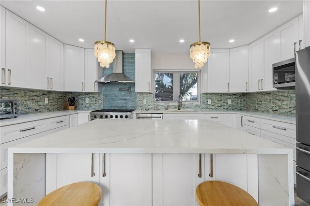 kitchen with a kitchen bar, white cabinetry, appliances with stainless steel finishes, and wall chimney exhaust hood