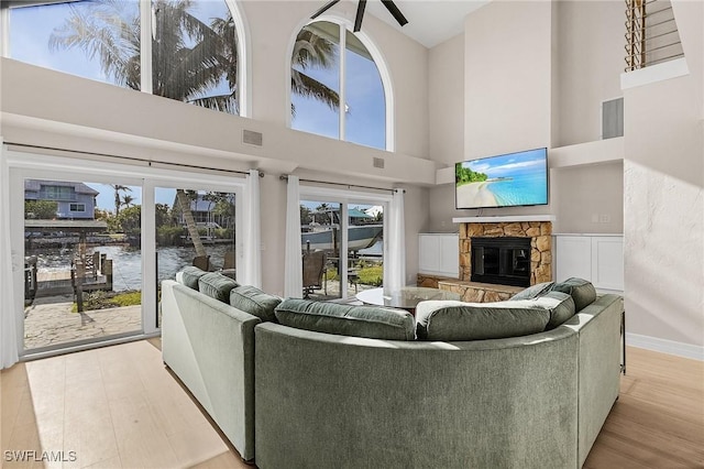 living room featuring a healthy amount of sunlight, a towering ceiling, a stone fireplace, and light hardwood / wood-style floors