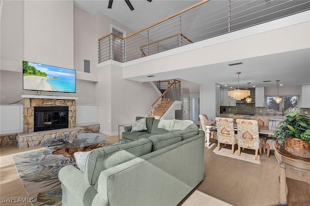 living room with light hardwood / wood-style flooring, ceiling fan with notable chandelier, a fireplace, and a high ceiling