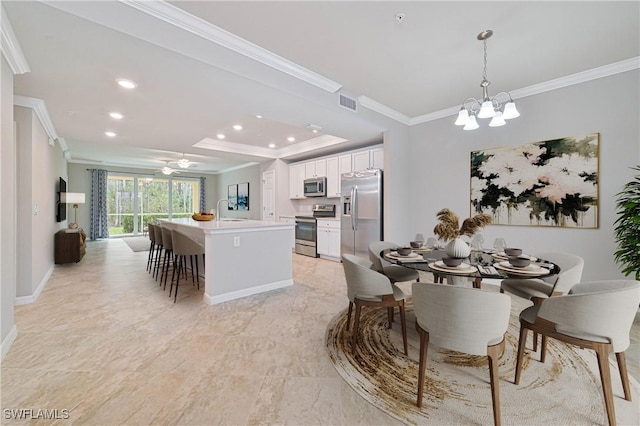 dining area with ceiling fan with notable chandelier, sink, a tray ceiling, and crown molding