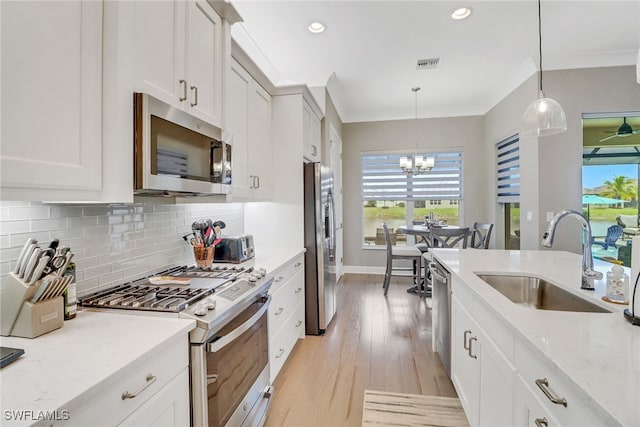 kitchen with light stone countertops, appliances with stainless steel finishes, white cabinetry, sink, and hanging light fixtures