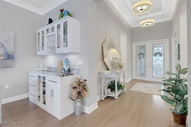 entrance foyer with ornamental molding, light hardwood / wood-style flooring, french doors, and a tray ceiling