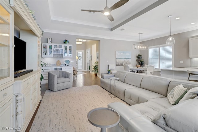 living room featuring a raised ceiling, crown molding, ceiling fan with notable chandelier, and light hardwood / wood-style floors