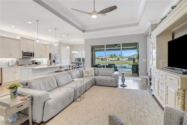 living room with a raised ceiling, ceiling fan with notable chandelier, and light hardwood / wood-style flooring