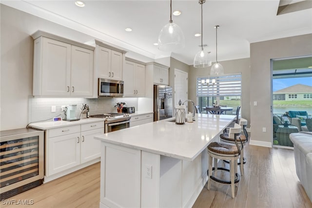 kitchen with pendant lighting, sink, a kitchen island with sink, stainless steel appliances, and beverage cooler