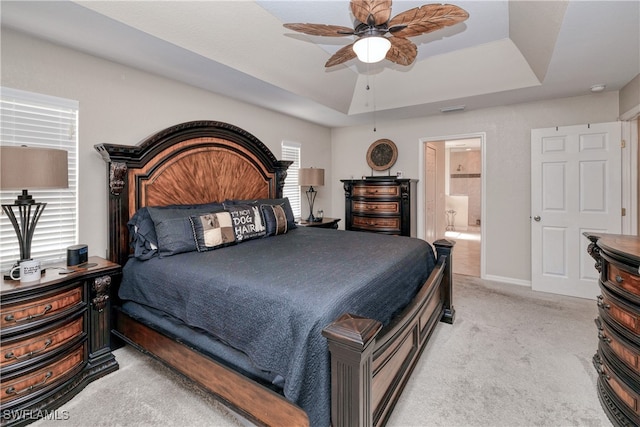 bedroom featuring ceiling fan, a tray ceiling, ensuite bath, and light carpet