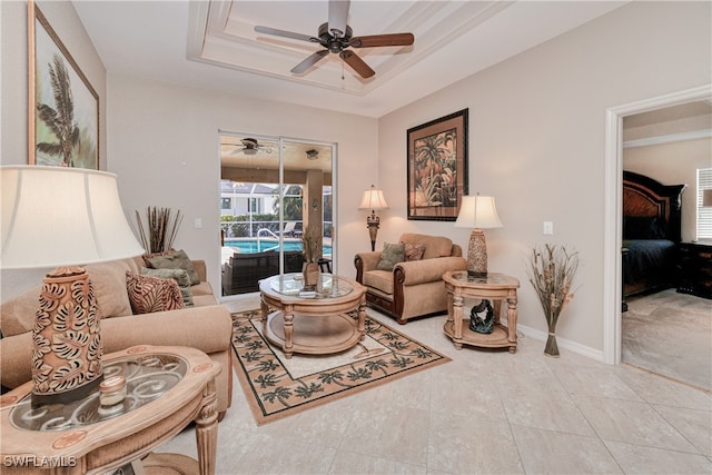 tiled living room with ceiling fan and a raised ceiling