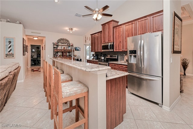 kitchen featuring a center island with sink, stainless steel appliances, decorative backsplash, a kitchen breakfast bar, and light stone counters