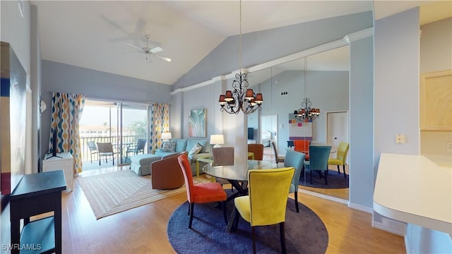 dining area with ceiling fan with notable chandelier, hardwood / wood-style flooring, and high vaulted ceiling