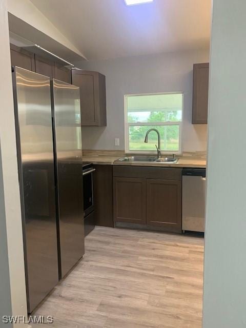 kitchen with sink, stainless steel appliances, light wood-type flooring, and vaulted ceiling