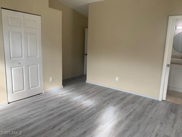 unfurnished bedroom featuring ensuite bath, a closet, and light hardwood / wood-style flooring